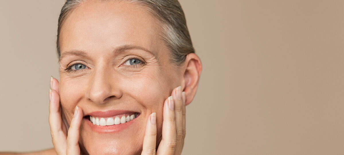 middle aged woman looking into camera with hands holding her face smiling after receiving treatment for skincare at feinstein dermatology in delray beach fl