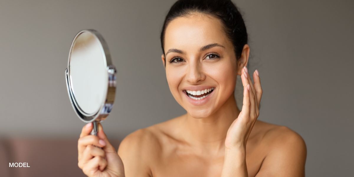 young woman happy smiling at the camera holding a mirror after a halo laser treatment at feinstein dermatology in delray beach fl